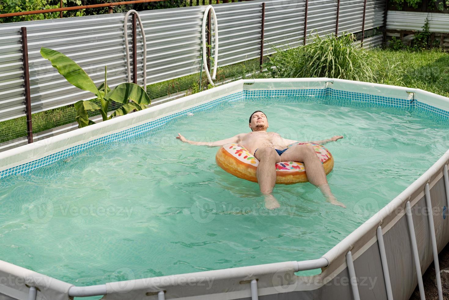 junger Mann schwimmt auf aufblasbarem Schwimmschlauch im Pool foto