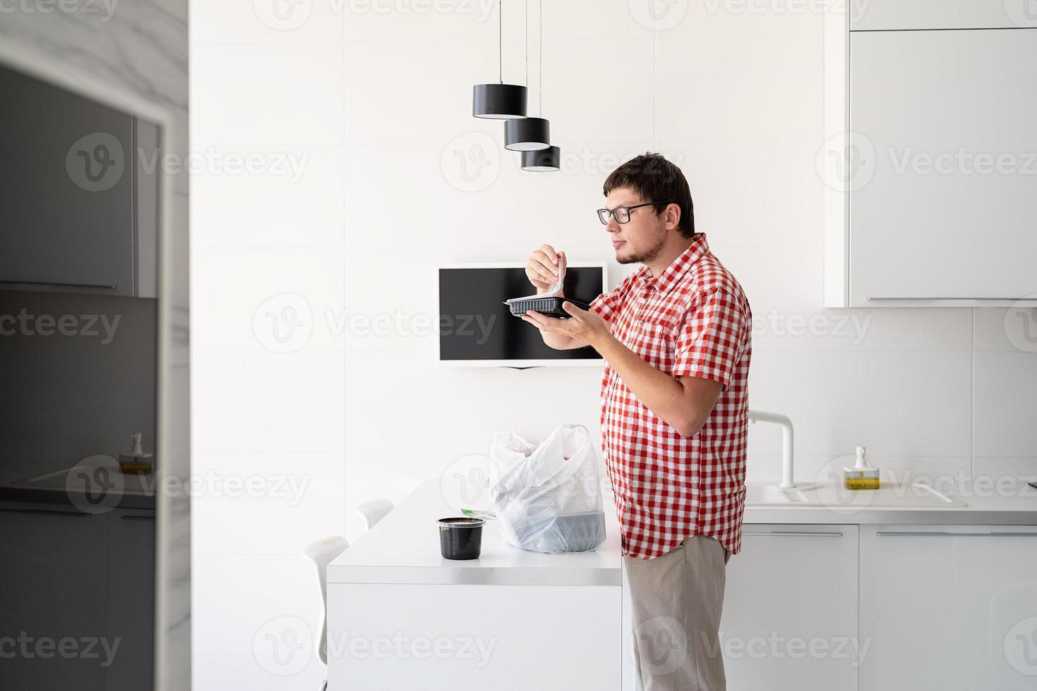 Mann, der eine Einweg-Plastiktüte mit Essenslieferung in der Küche hält foto