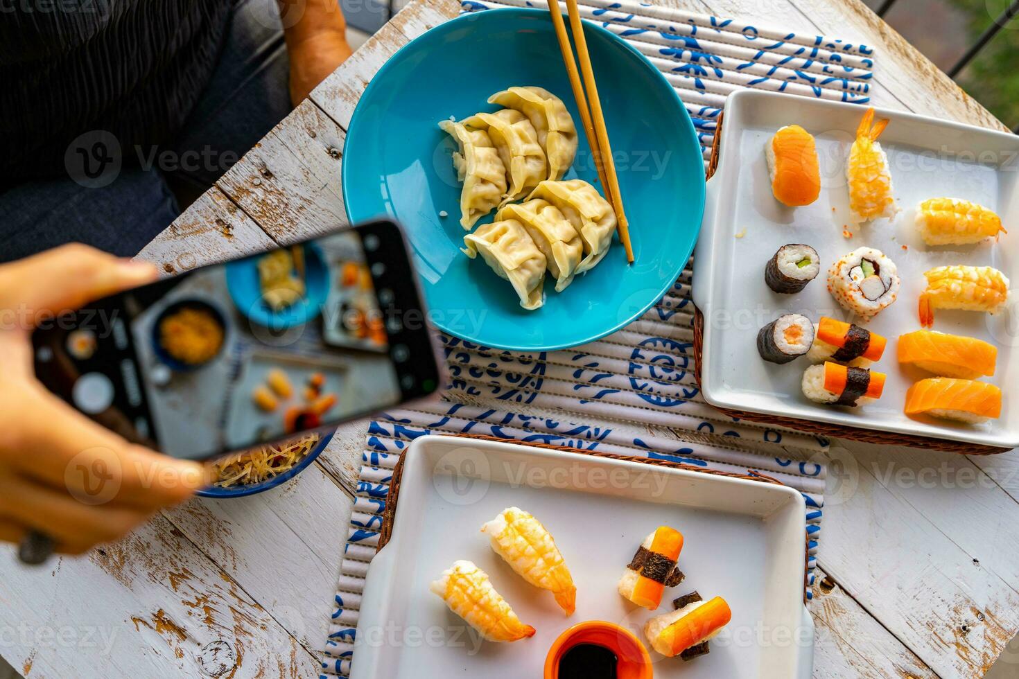 Frau Fotografieren mit Smartphone von über von verschiedene Chinesisch Lebensmittel im bunt Schalen auf ein hölzern Tabelle foto