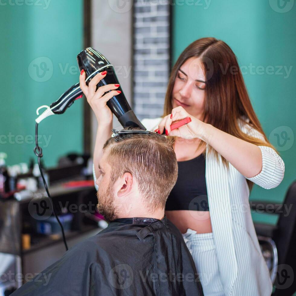 Mädchen Friseur trocknet Haar zu ein Mann im ein Salon foto