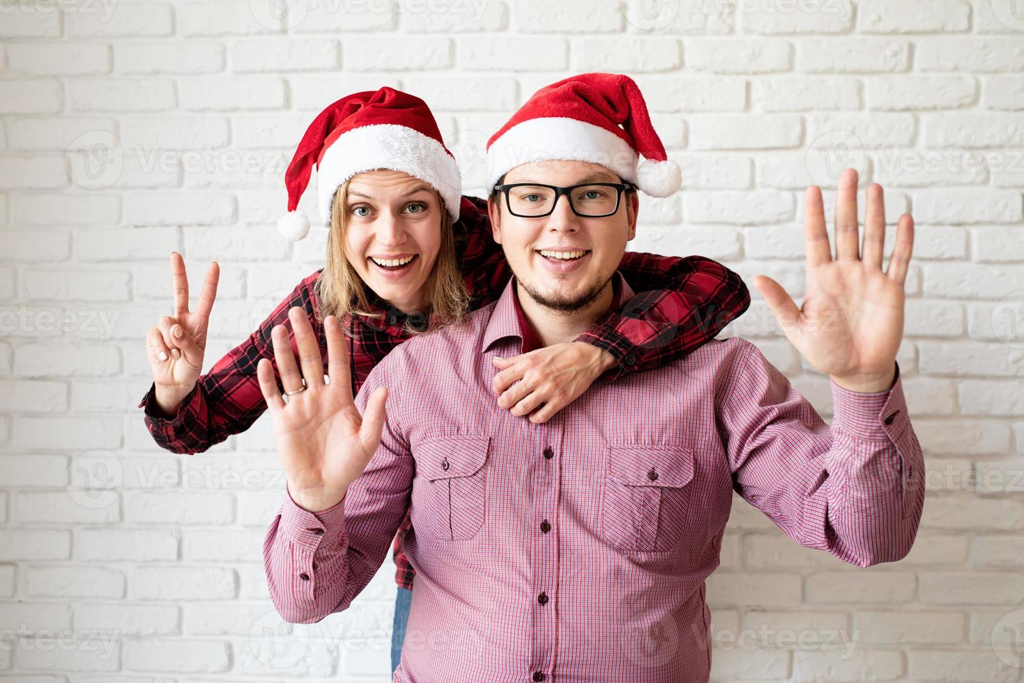 glückliches weihnachtspaar in weihnachtsmützen auf weißem backsteinmauerhintergrund foto