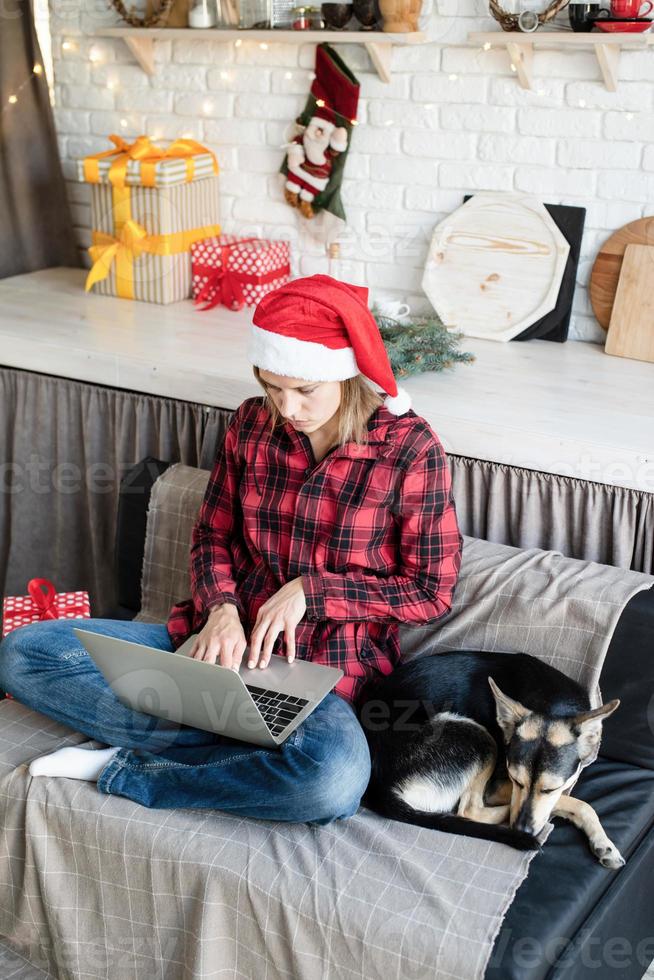 junge blonde Frau in Weihnachtsmütze arbeitet am Laptop foto