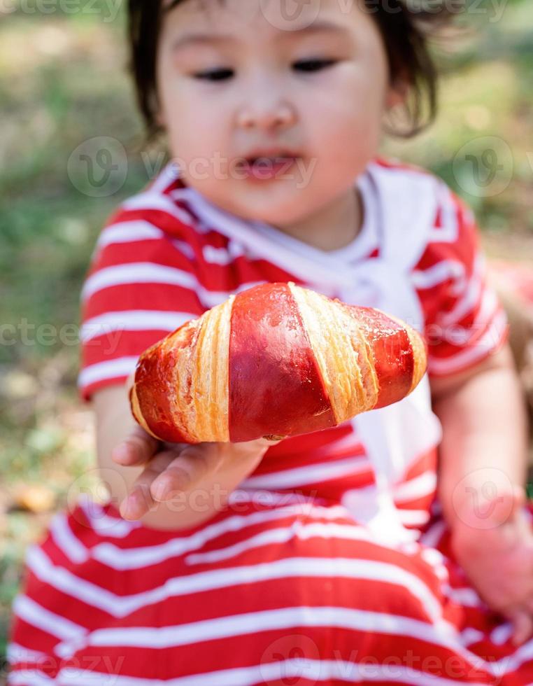 süßes kleines Baby in einem roten Kleid und Strohhut bei einem Picknick im Park foto