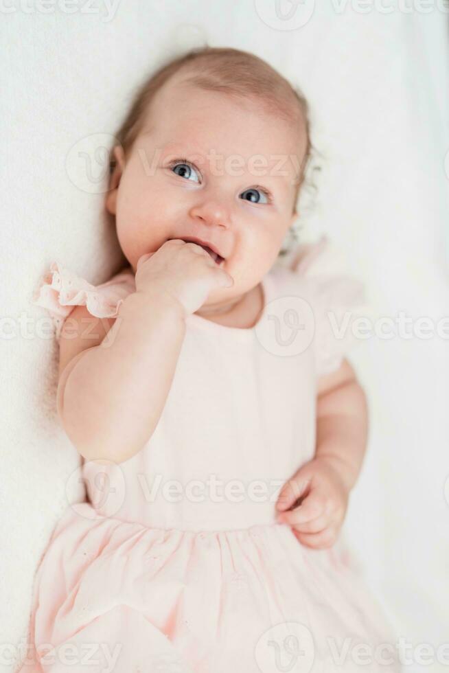 Porträt von ein schön Baby Mädchen Lügen auf ein Weiß Blatt im ihr Zimmer foto