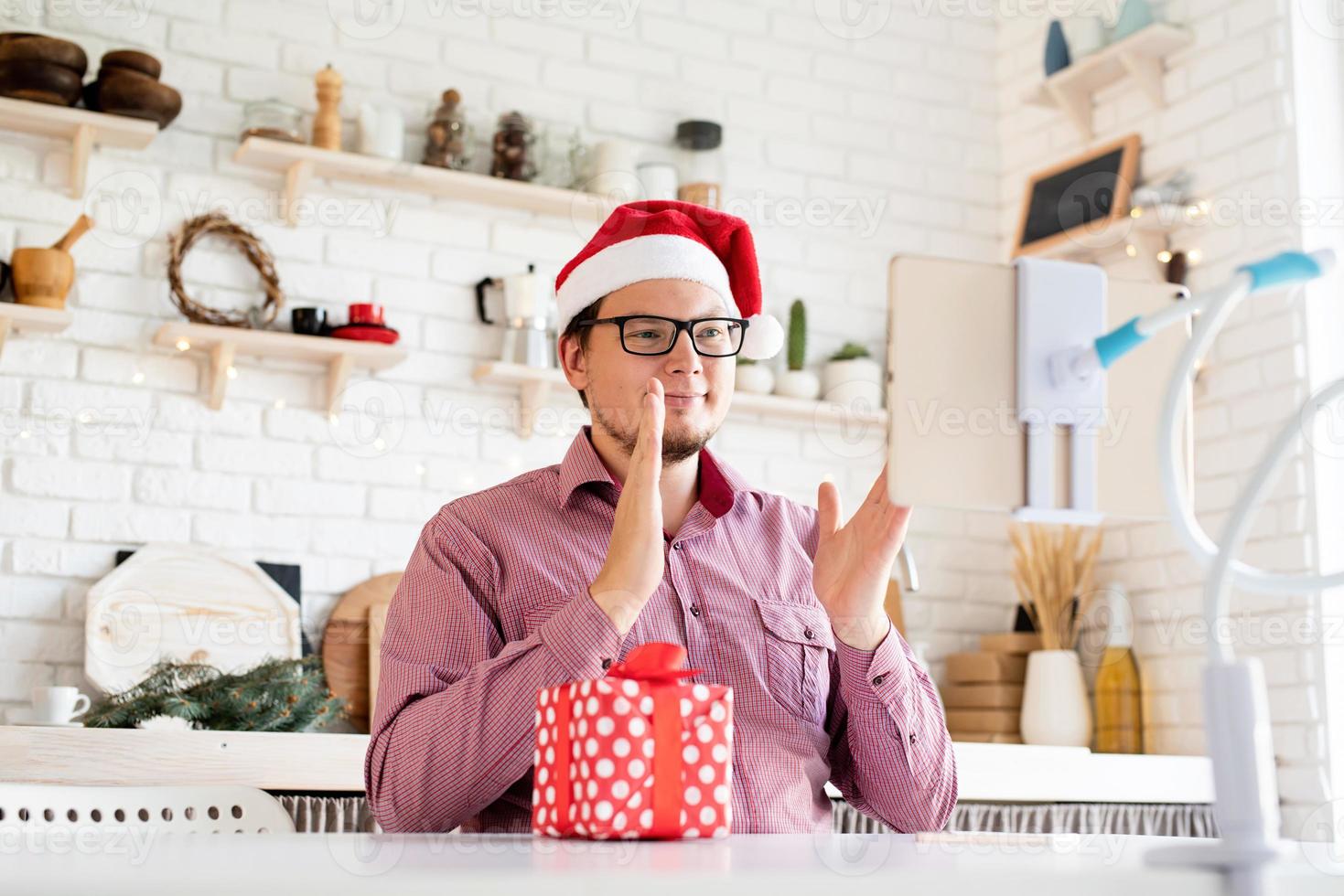 junger Mann in Weihnachtsmütze grüßt seine Freunde im Video-Chat auf dem Tablet foto