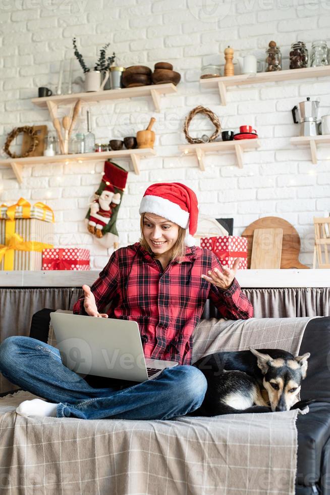 Frau mit Weihnachtsmütze begrüßt ihre Freunde im Video-Chat auf dem Laptop foto