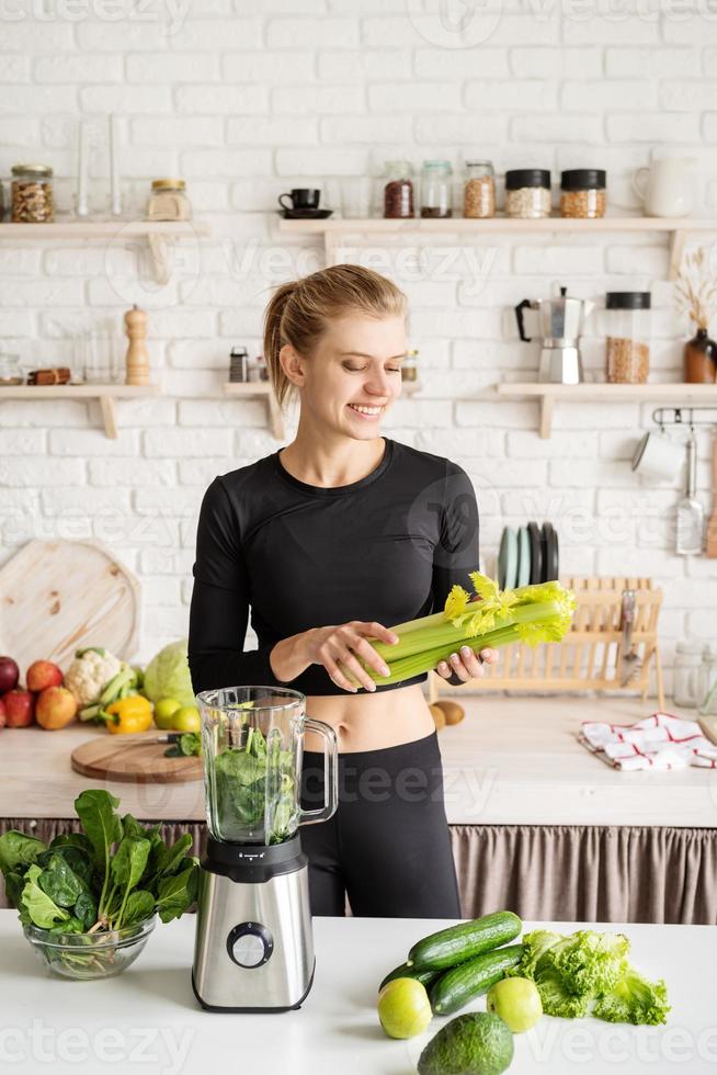 junge blonde lächelnde Frau macht Sellerie-Smoothie zu Hause in der Küche foto