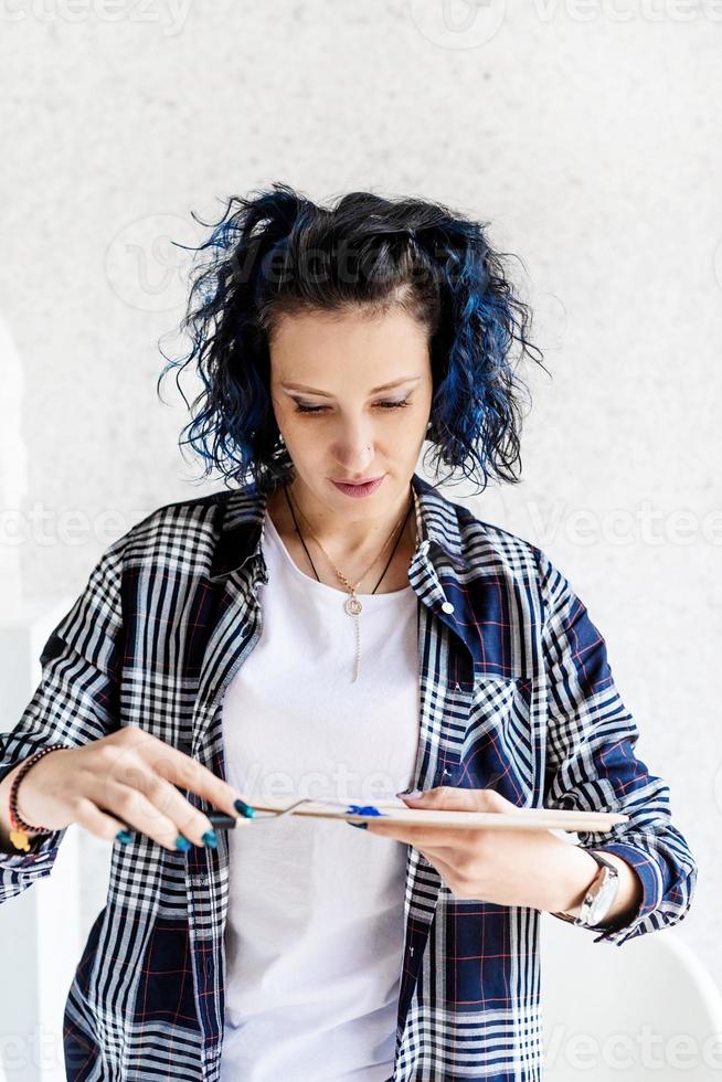 Kreative Frau mit blau gefärbten Haaren malt in ihrem Atelier foto