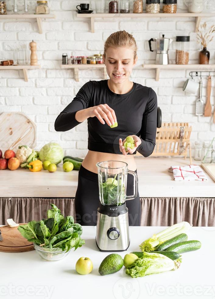 junge blonde lächelnde Frau macht Sellerie-Smoothie zu Hause in der Küche foto