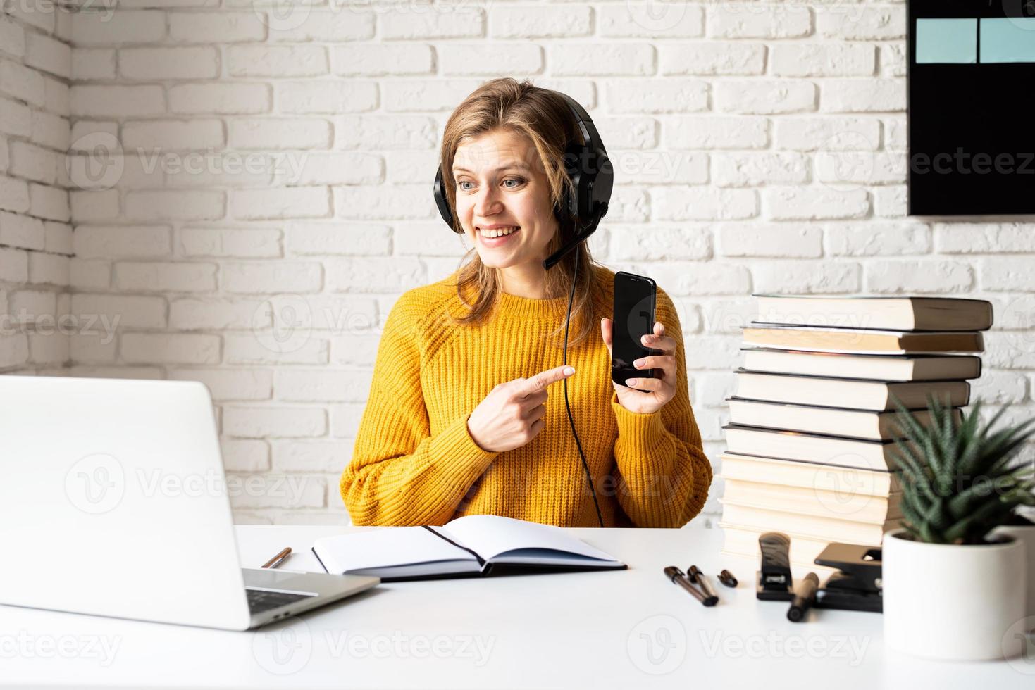 Frau, die online mit Laptop studiert, der Handy zeigt foto