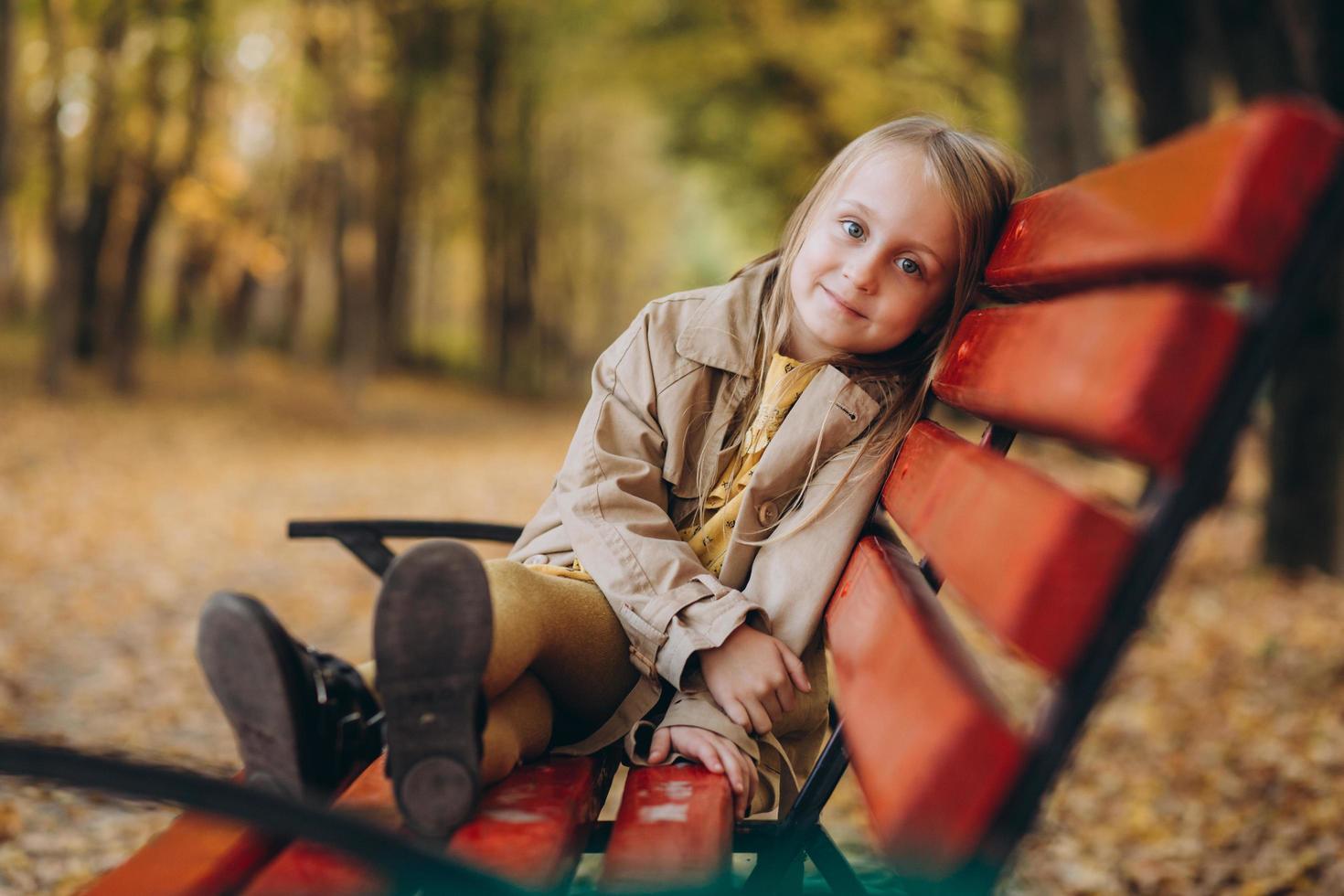 ein kleines mädchen in einem gelben kleid und beige mantel spaziert im herbstpark foto