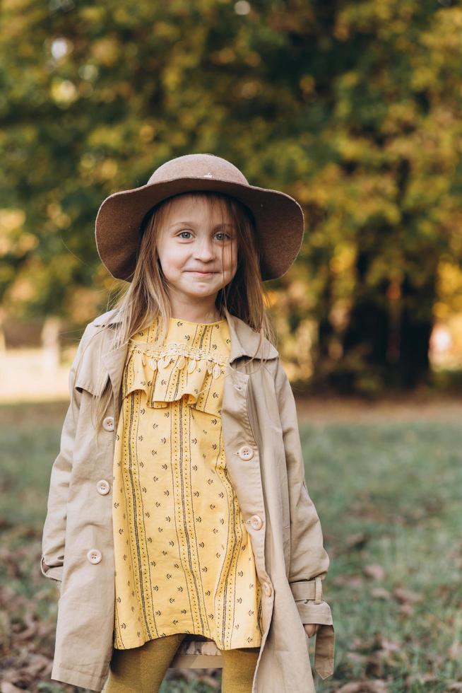 ein kleines mädchen in einem gelben kleid und beige mantel spaziert im herbstpark foto