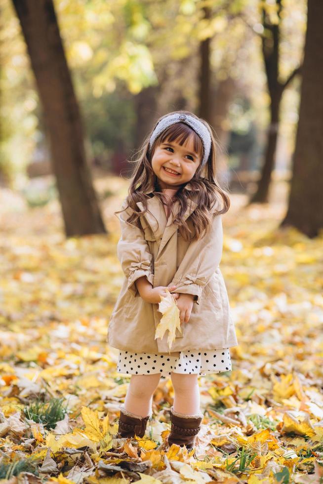 glückliches kleines Mädchen, das ein gelbes Ahornblatt im Herbstpark hält foto