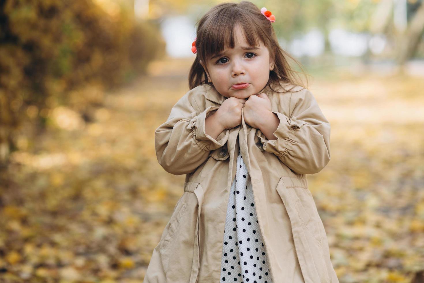 kleines Mädchen in einem beigen Mantel zeigt Emotionen im Herbstpark foto