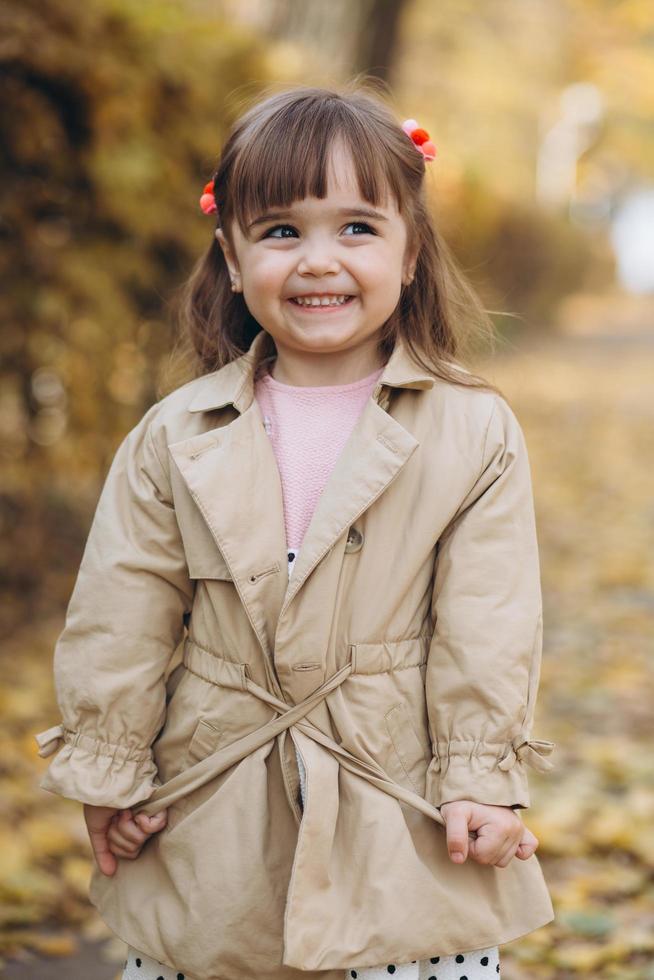 Schönes kleines Mädchen in einem beigefarbenen Mantel geht im Herbstpark spazieren foto