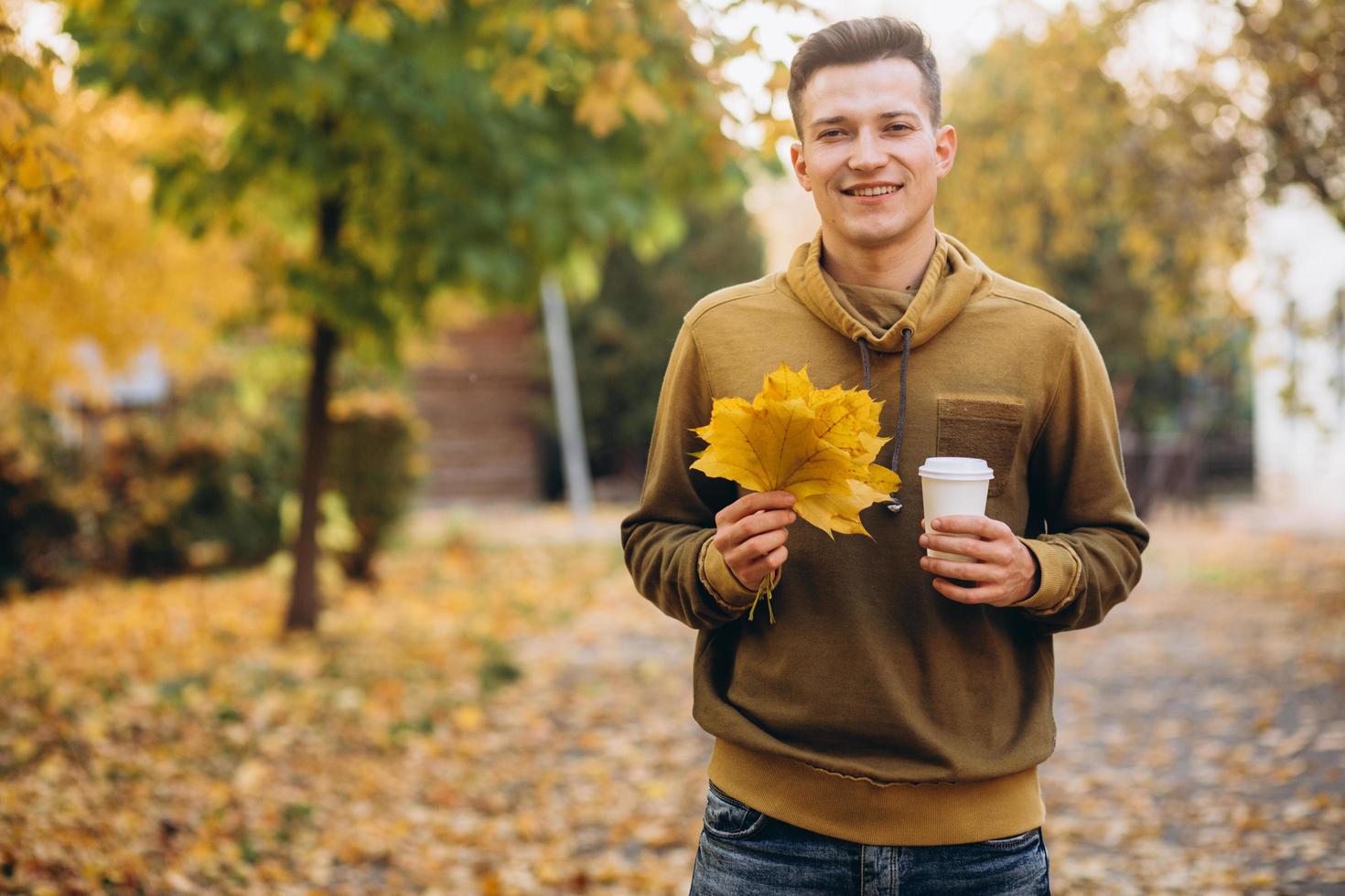 Kerl lächelt und hält einen Blumenstrauß und eine Tasse Kaffee im Park? foto