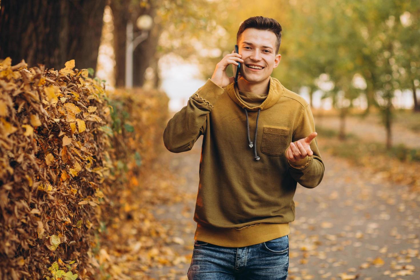 glücklicher Kerl, der im Herbstpark lächelt und telefoniert? foto