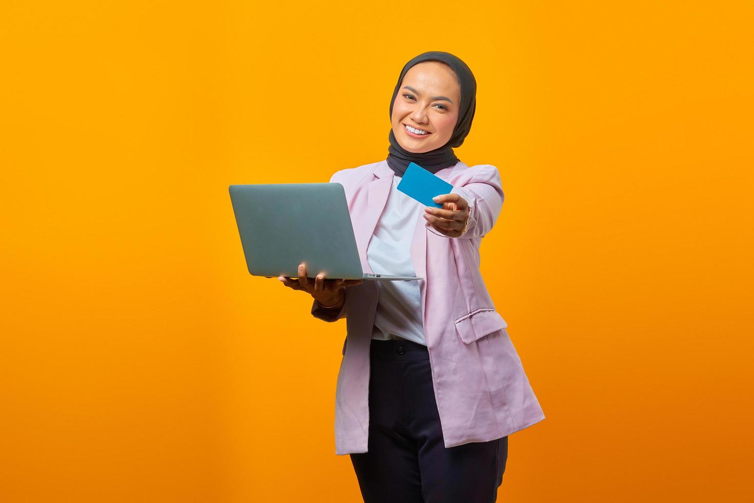 fröhliche junge Frau, die mit Laptop steht und Kreditkarte zeigt foto
