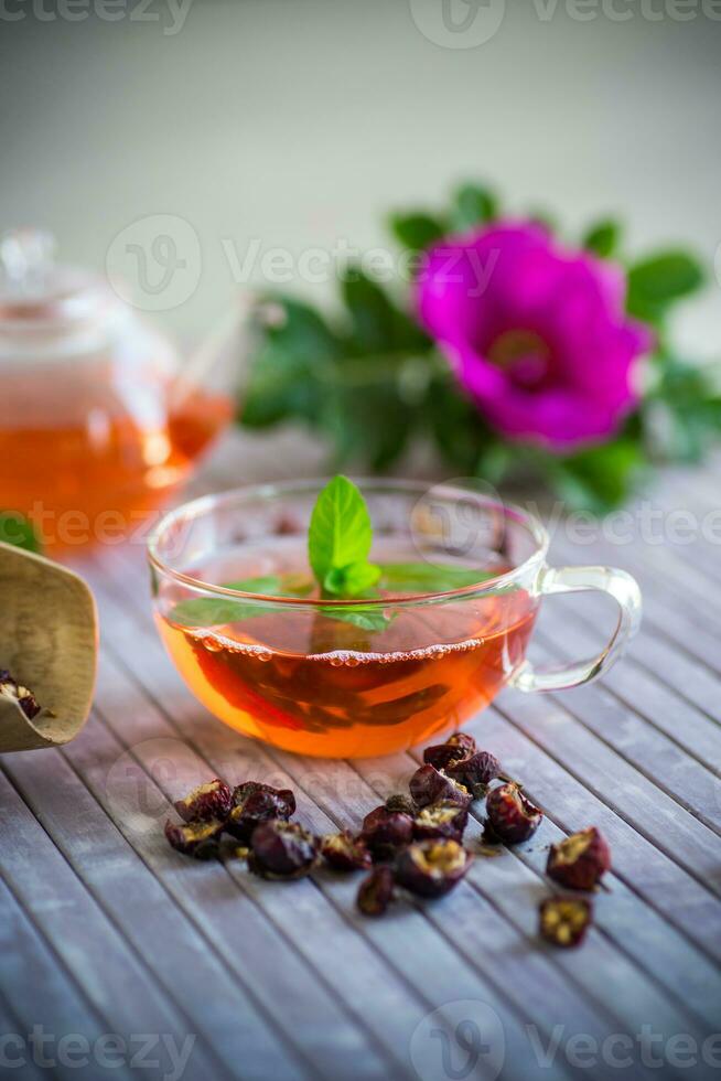 gebraut Hagebutte Tee im ein Glas Teekanne mit Hagebutte Blumen und Minze foto
