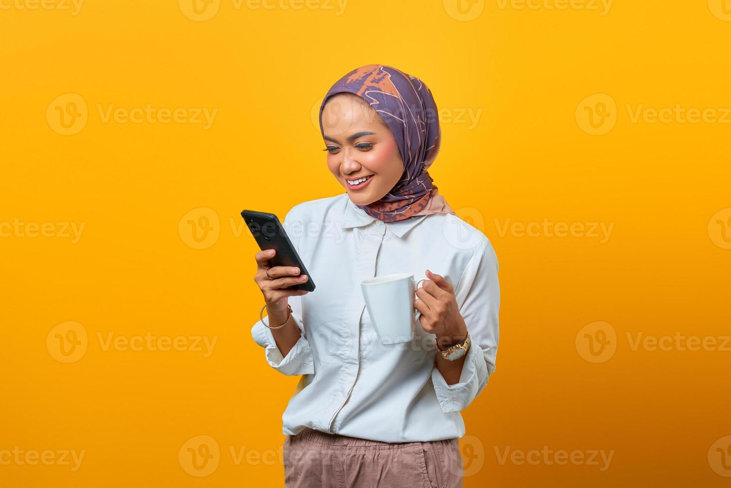 asiatische Frau, die sich entspannt, Tasse hält und Handy benutzt foto
