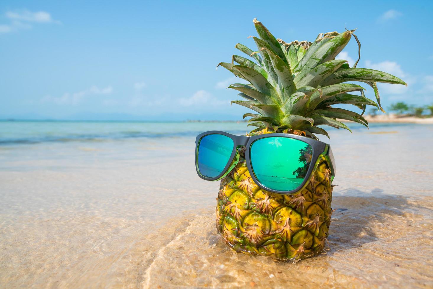 Ananas mit Sonnenbrille auf tropischem Strandhintergrund. Sommerkonzept foto