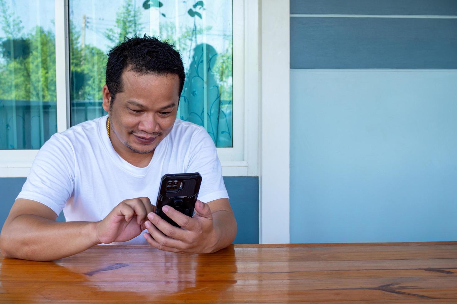 asiatischer Mann mit weißem Hemd, der das Telefon auf einem Holztisch benutzt foto