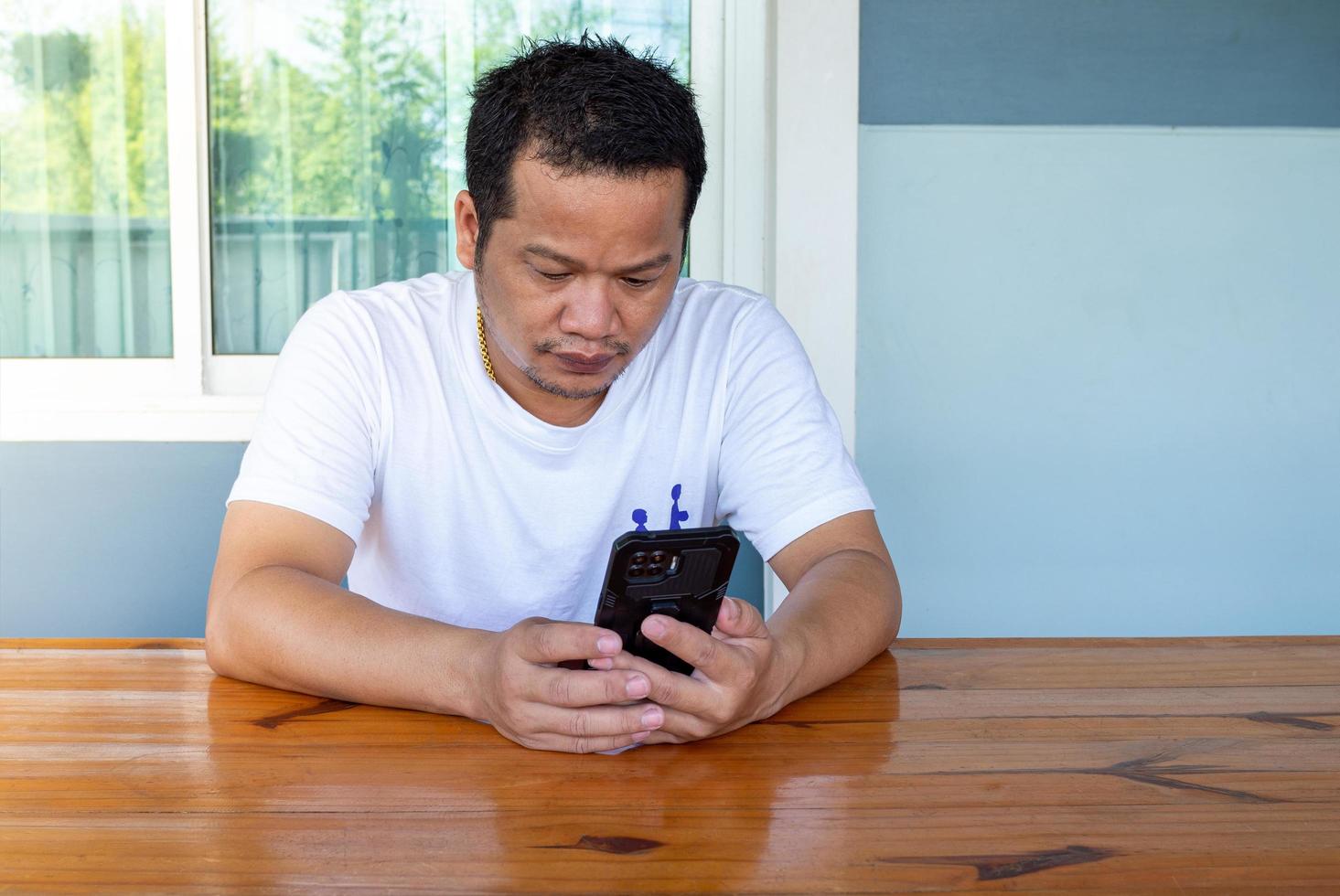 asiatischer Mann mit weißem Hemd, der das Telefon auf einem Holztisch benutzt foto