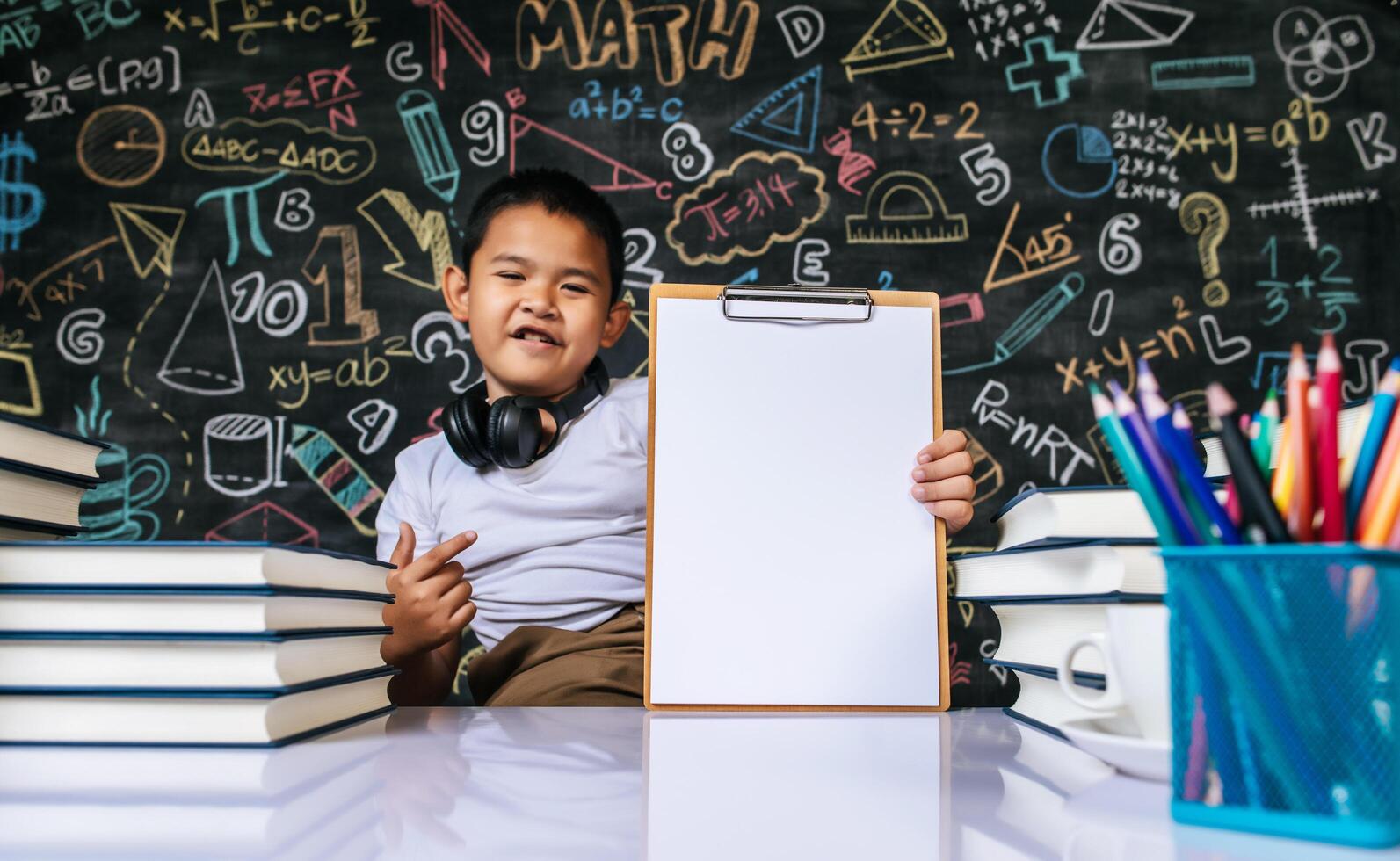 Kind sitzt und zeigt Klemmbrett im Klassenzimmer foto