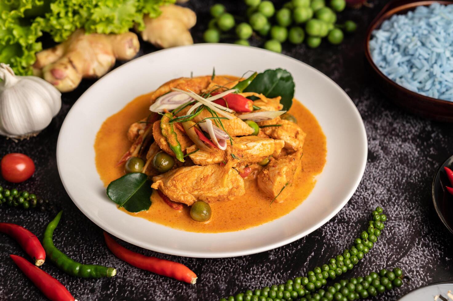 trockenes grünes Curry mit Hühnchen in weißen Tellern auf schwarzem Zement foto