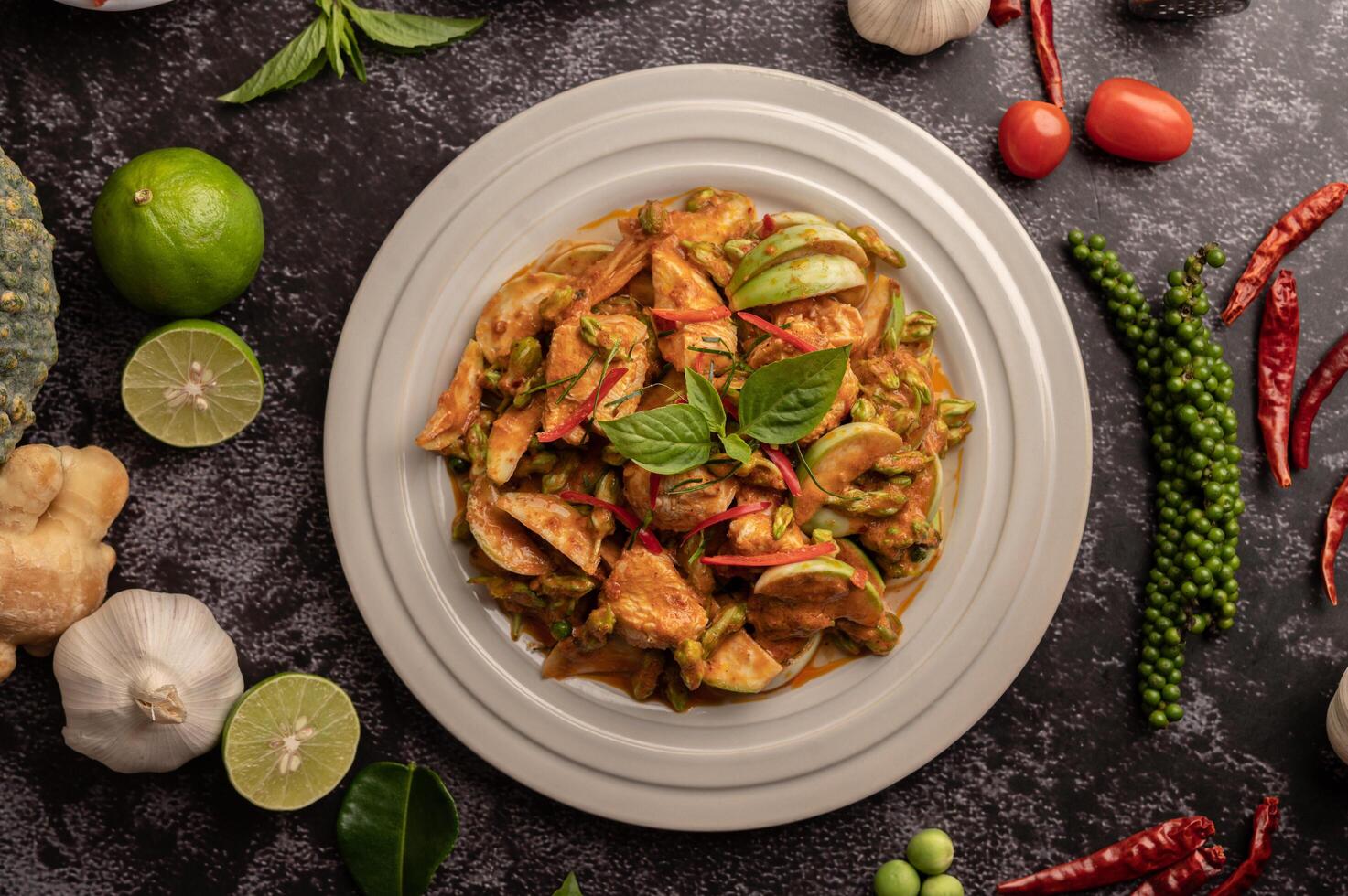 trockenes grünes Curry mit Hühnchen in weißen Tellern auf schwarzem Zement foto