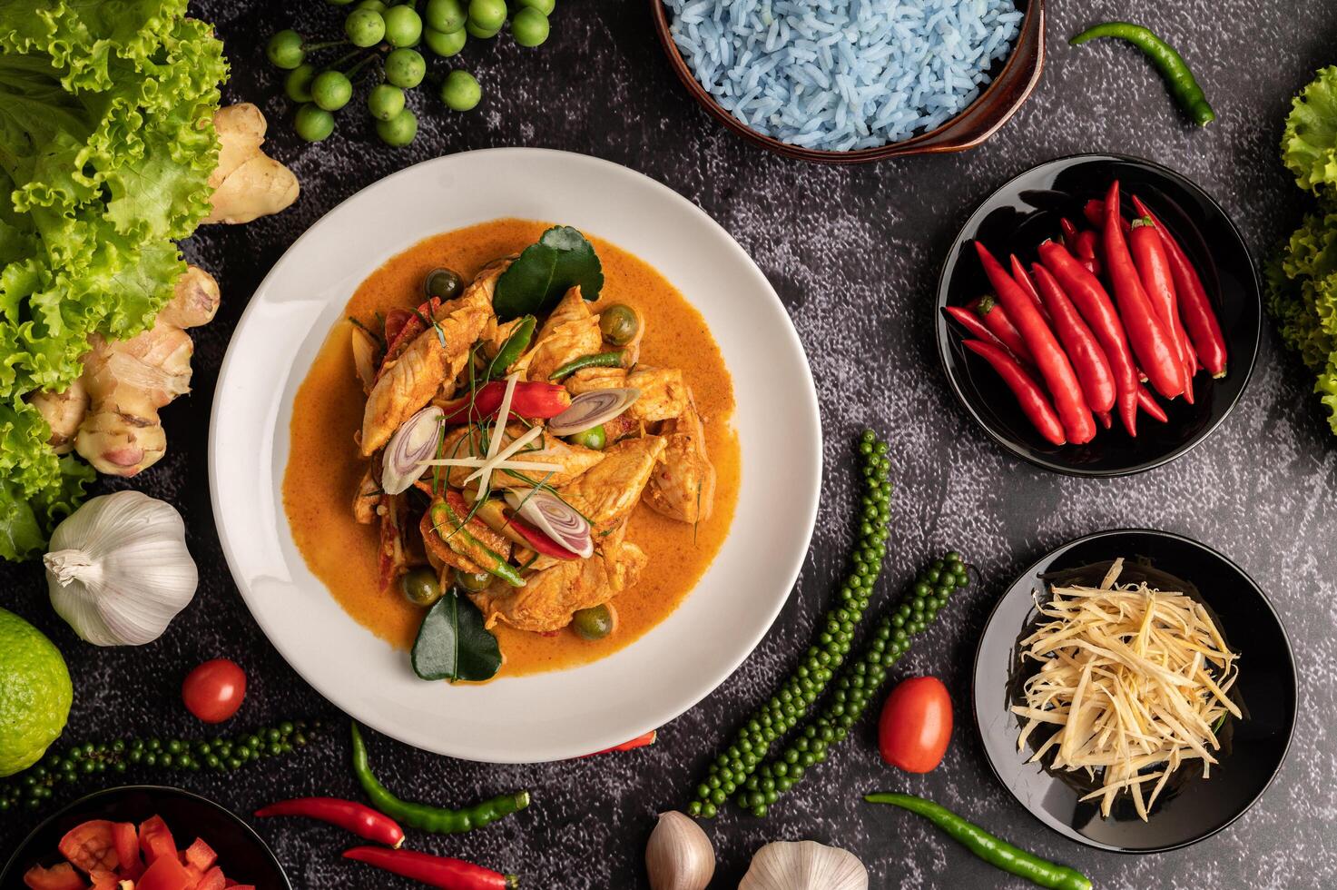 trockenes grünes Curry mit Hühnchen in weißen Tellern auf schwarzem Zement foto