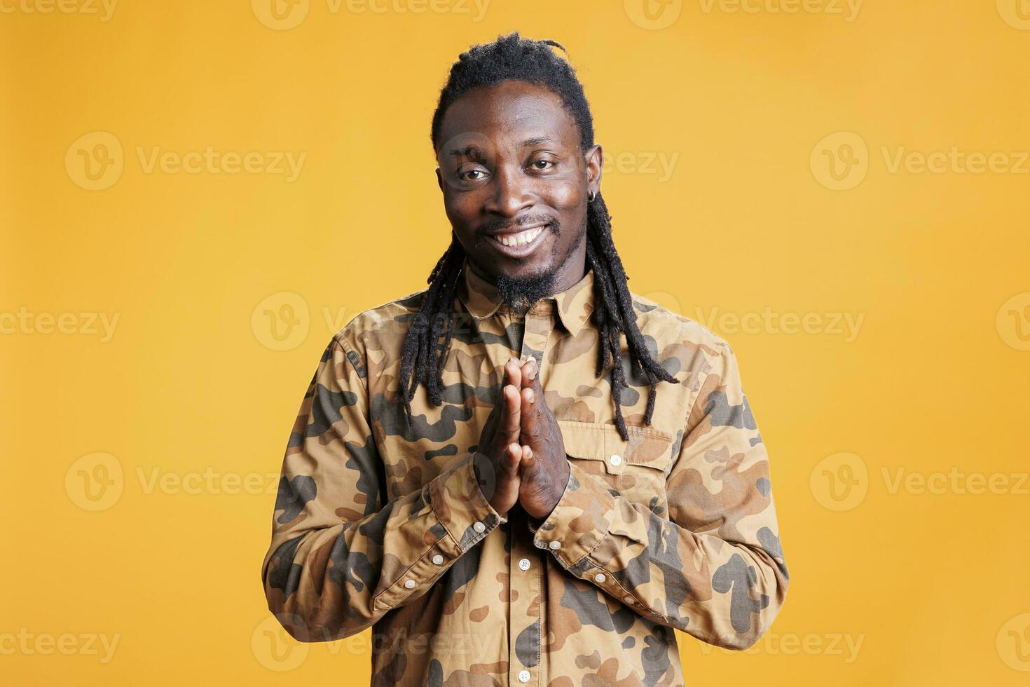 glücklich afrikanisch amerikanisch Person halten Palmen zusammen, fragen zum etwas im Studio Über Gelb Hintergrund. lächelnd Mann feiern Erfolg, applaudieren Menschen nach Arbeit Leistung foto