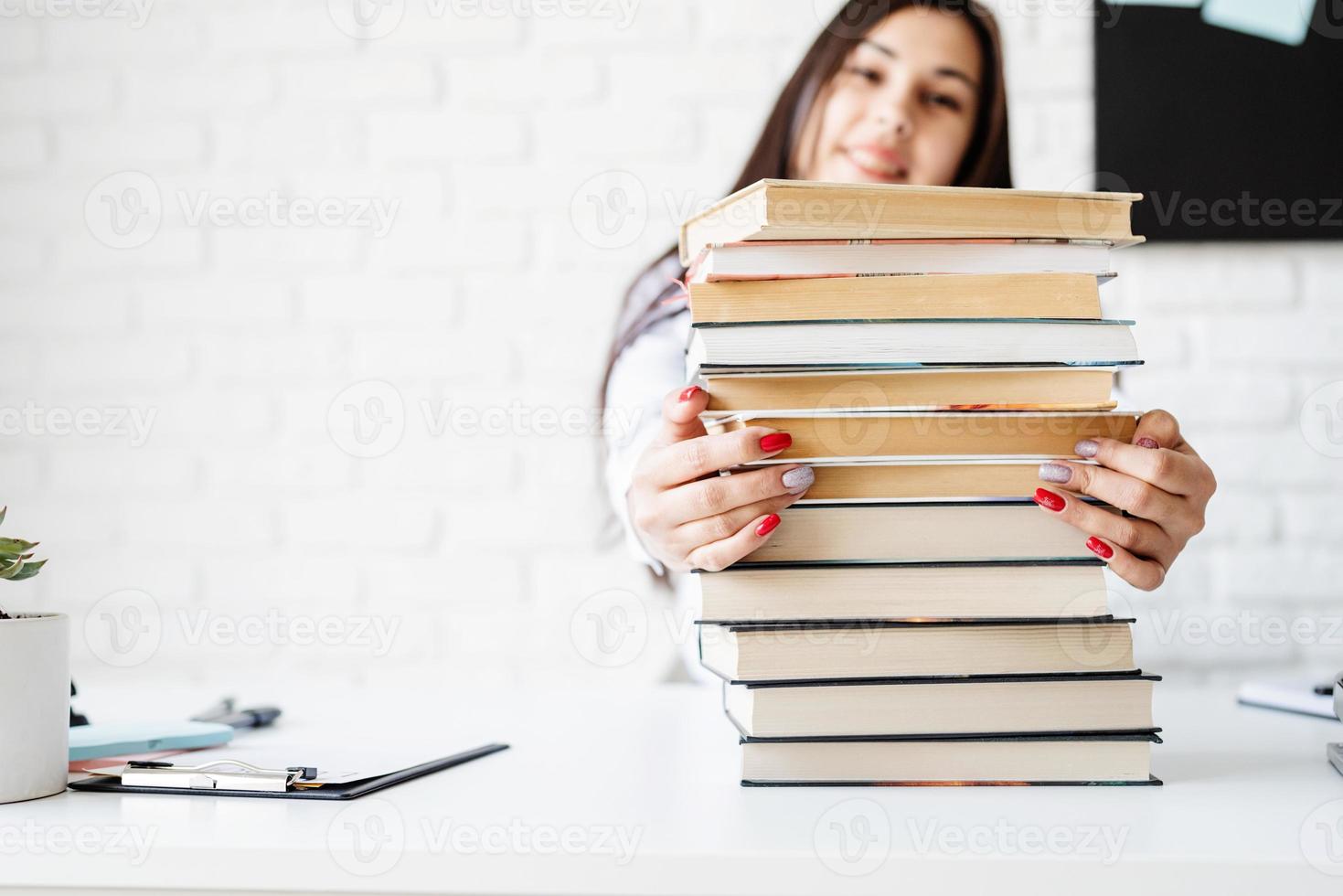 junge Lehrerin sitzt mit einem Stapel Bücher und schaut weg, bereit für den Unterricht? foto