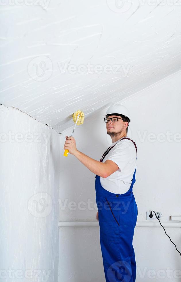 junger Mann in blauen Overalls und weißer Schutzhelm-Malwand foto