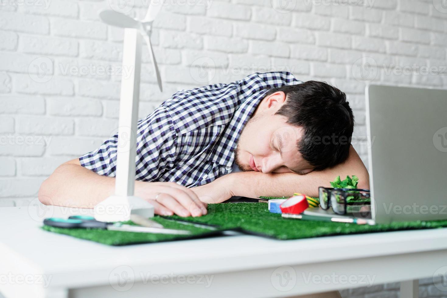 müder junger Mann, der auf seinem Schreibtisch schläft. Projekt-Dummy für erneuerbare Energien foto