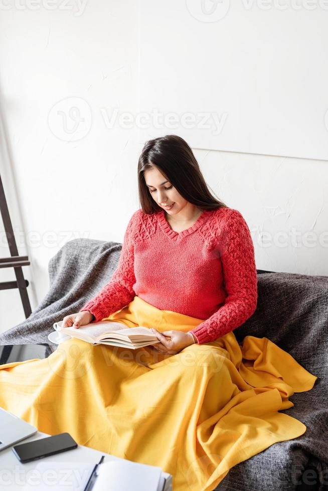Frau, die zu Hause ein Buch liest, sitzt auf dem Sofa und lächelt vor Freude foto