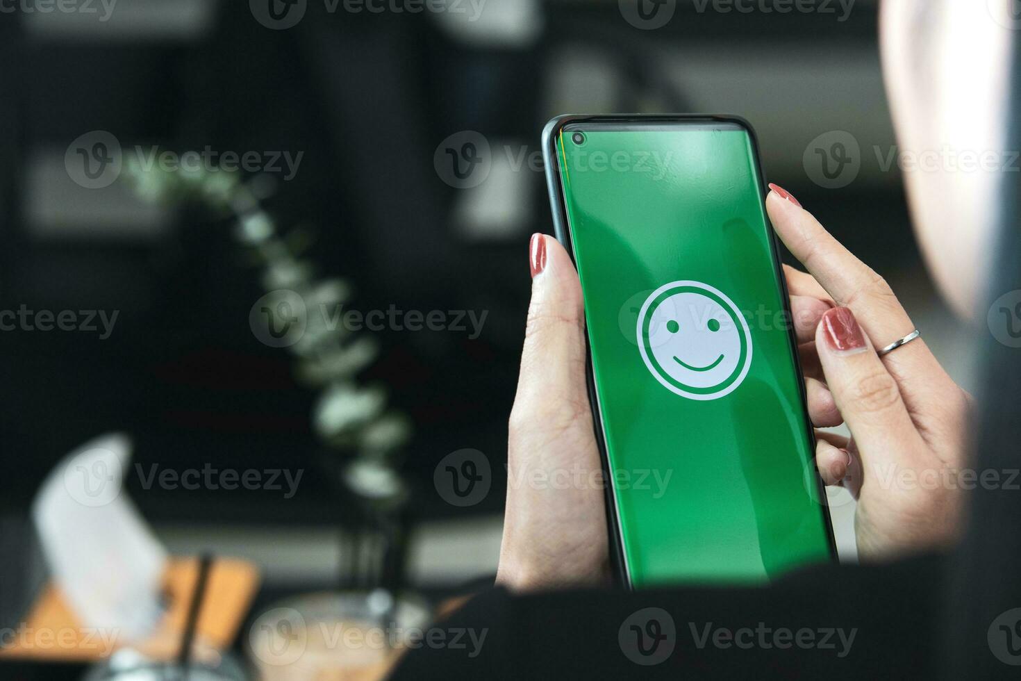 Frau hält ein Smartphone mit glücklich Emoticons auf das Bildschirm beim ein Restaurant. Konzept von auswerten Kunde Befriedigung beim sehr gut Niveau von Kunde Bedienung foto