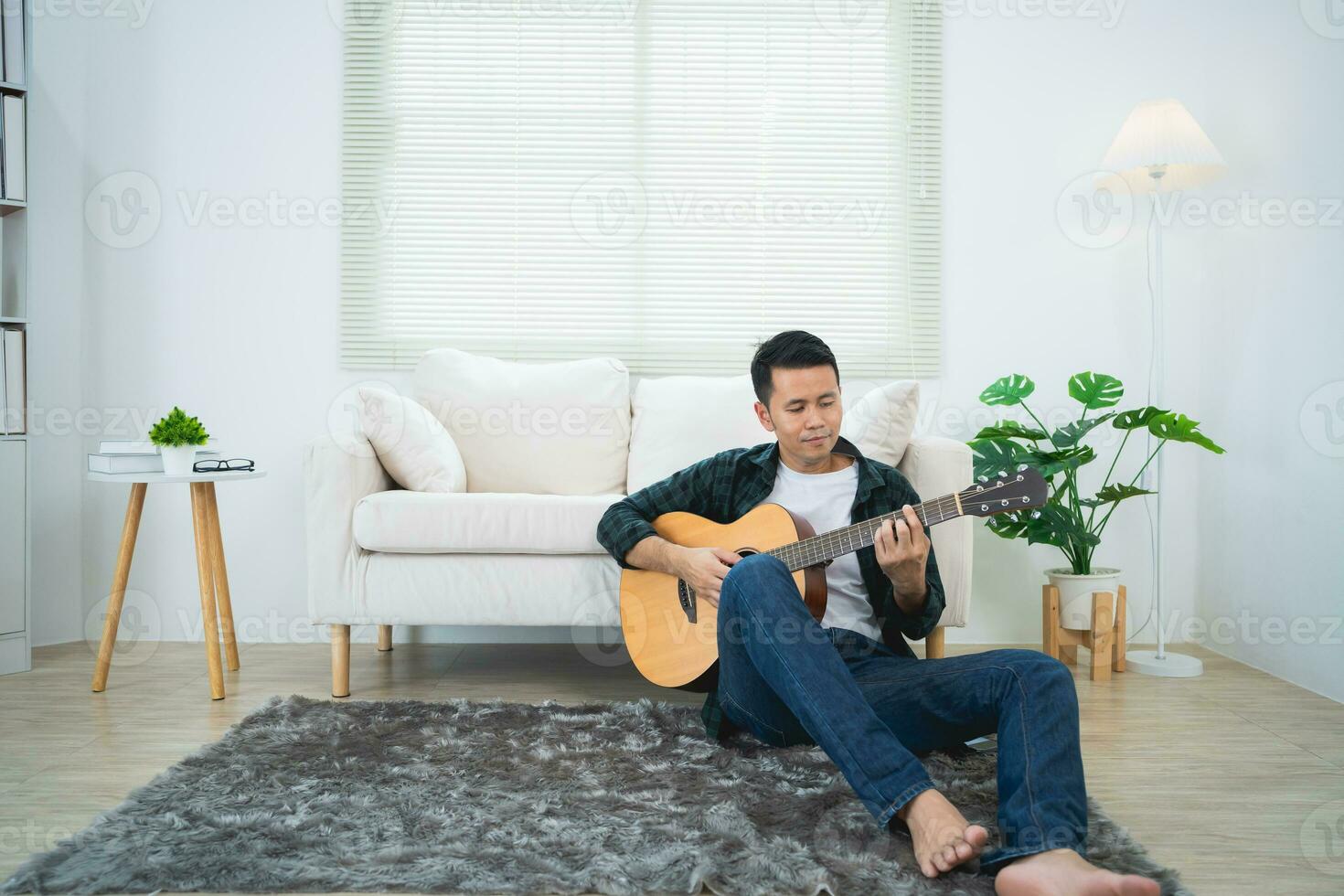 asiatisch Mann spielen Gitarre Sitzung auf Sofa Couch oder Fußboden im das Leben Zimmer beim heim. asiatisch Mann Schreiben Lied während spielen Gitarre beim heim. komponieren Lied Musik- Konzept. foto