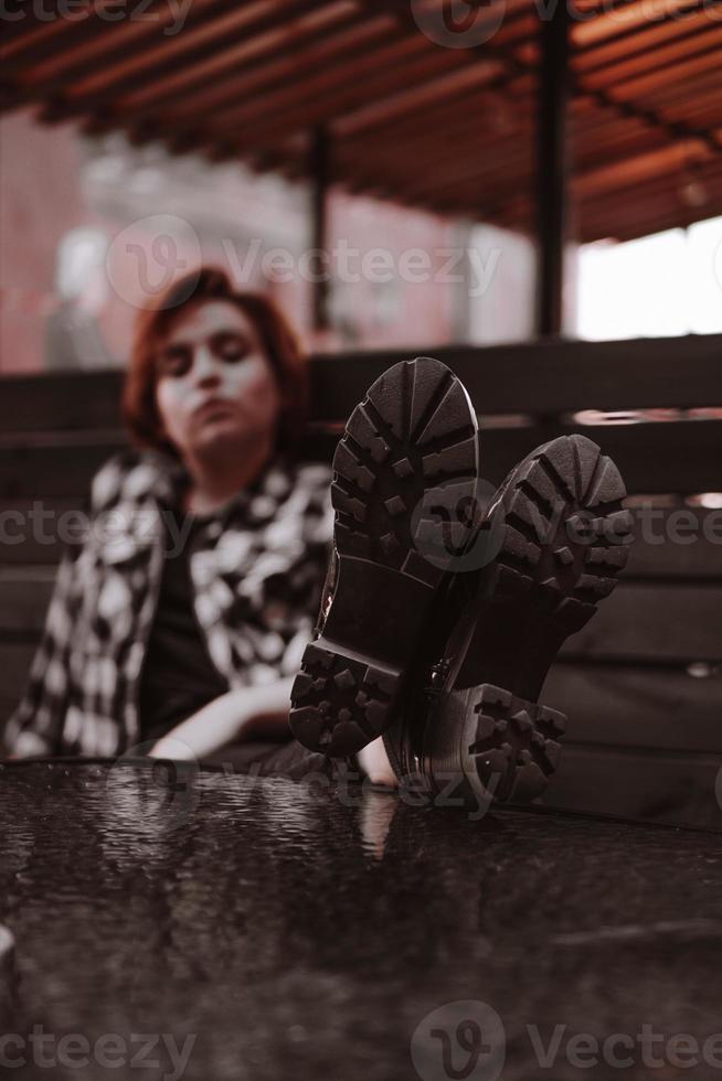 junge Frau mit kurzen roten Haaren in einer Bar legte ihre Beine auf den Tisch foto