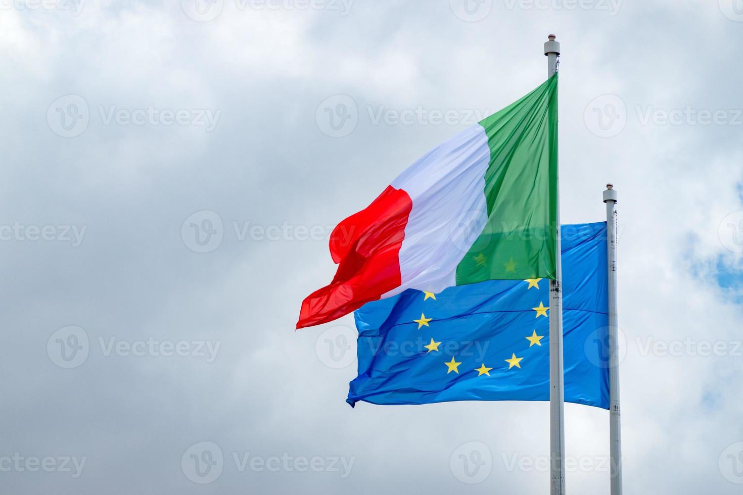 Flaggen der italienischen und europäischen Union wehen gegen einen bewölkten Himmel foto