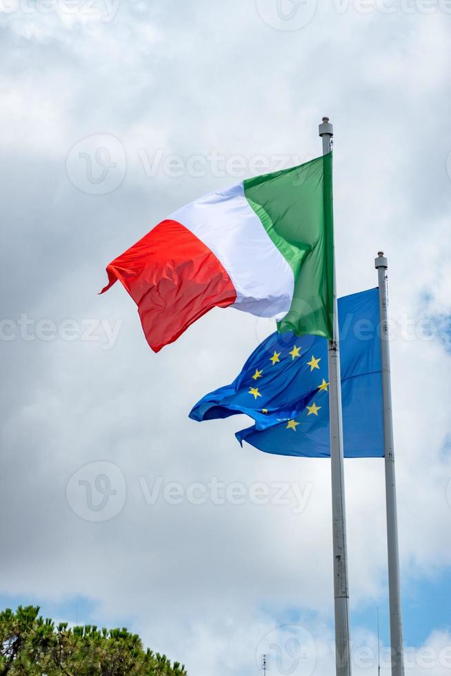 Flaggen der italienischen und europäischen Union wehen gegen einen bewölkten Himmel foto