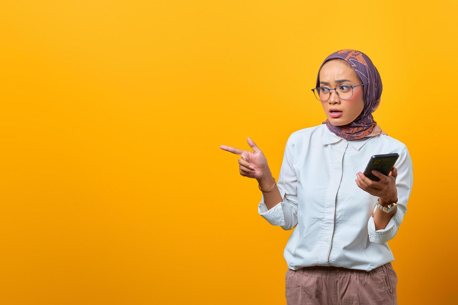 schockierte asiatische frau, die mit dem finger auf eine leere stelle zeigt foto