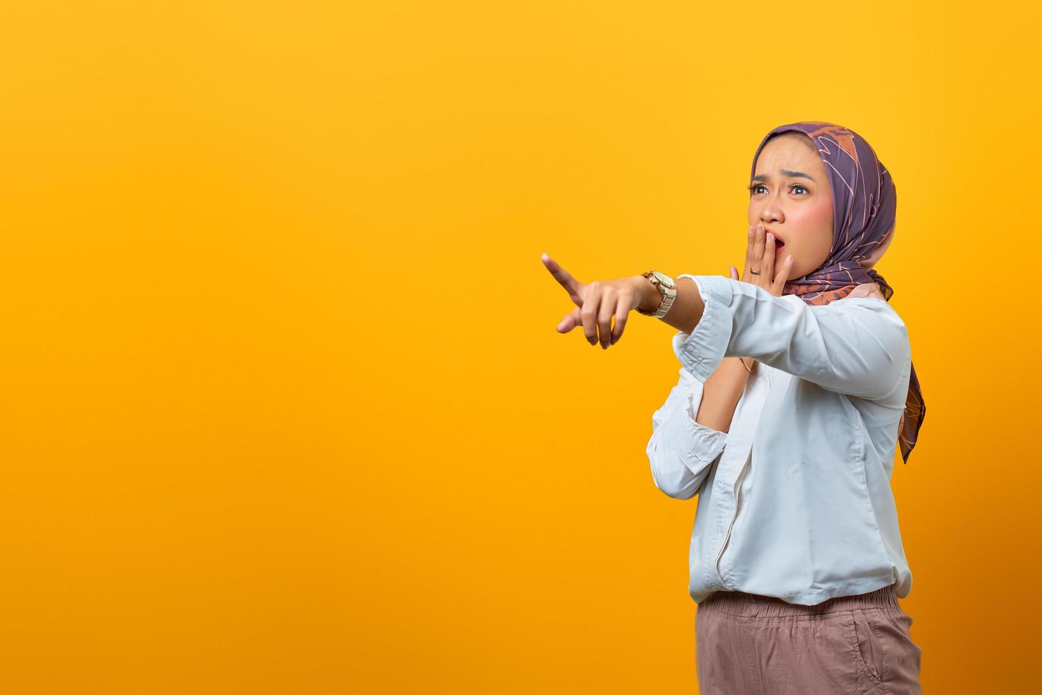 Porträt einer überraschten asiatischen Frau, die mit dem Finger auf eine Leerstelle zeigt foto