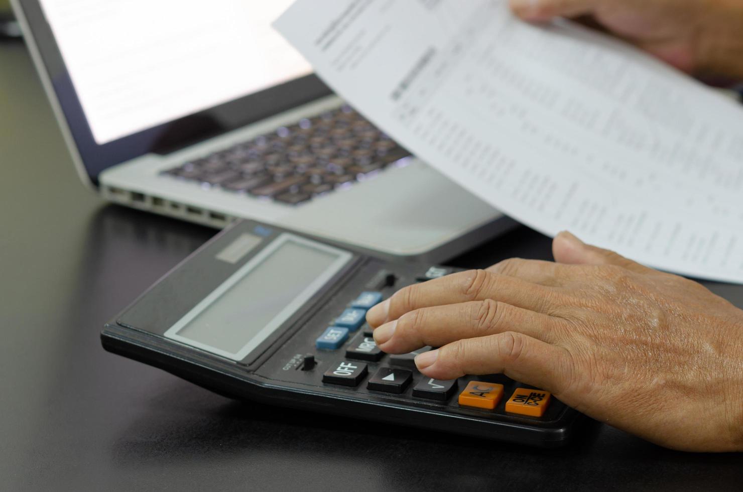 Geschäftsmann mit Taschenrechner an einem Schreibtisch. Unternehmensfinanzierung, Steuern, foto