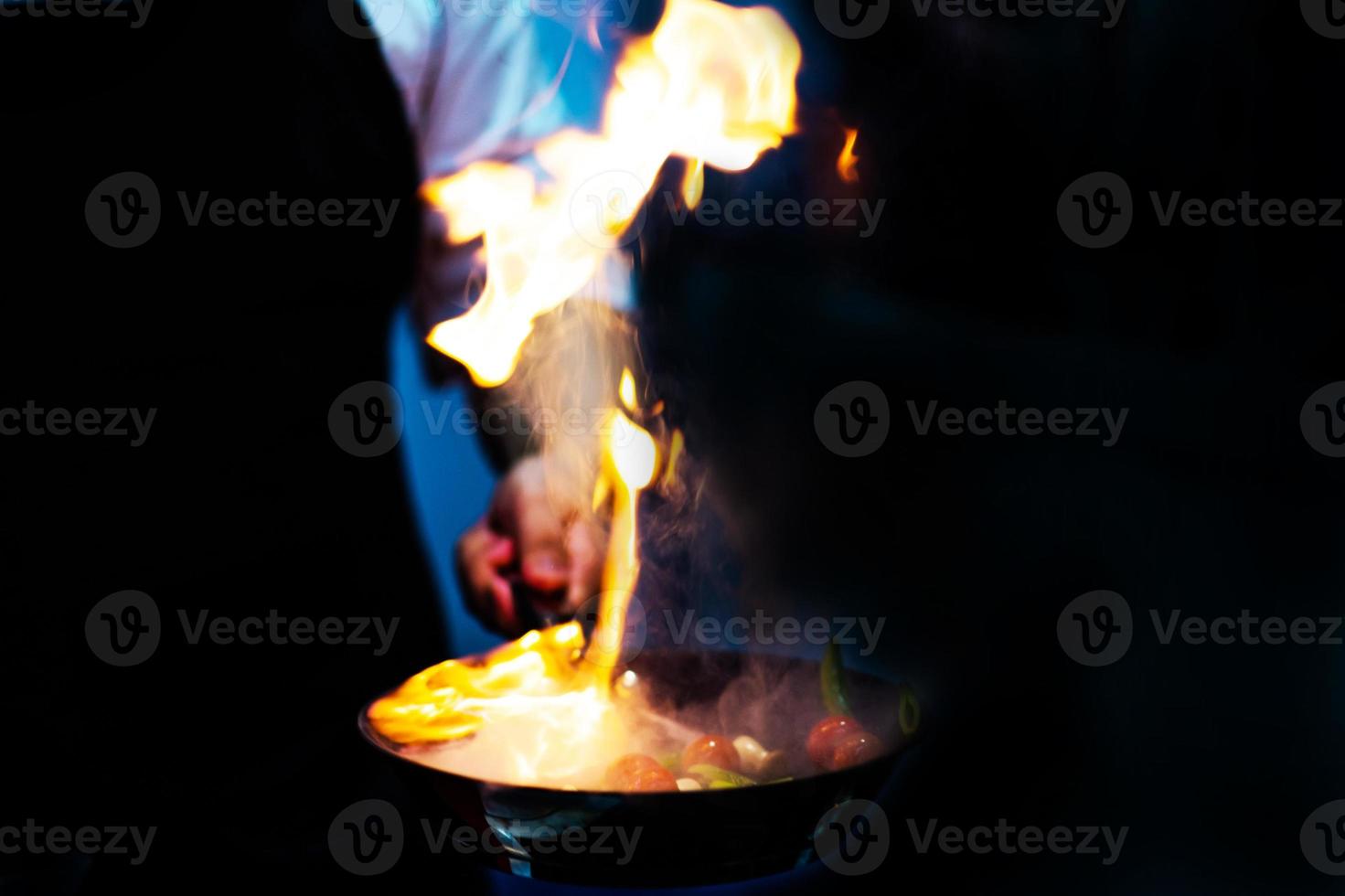 Koch kocht mit Flamme in einer Pfanne auf einem Küchenherd foto