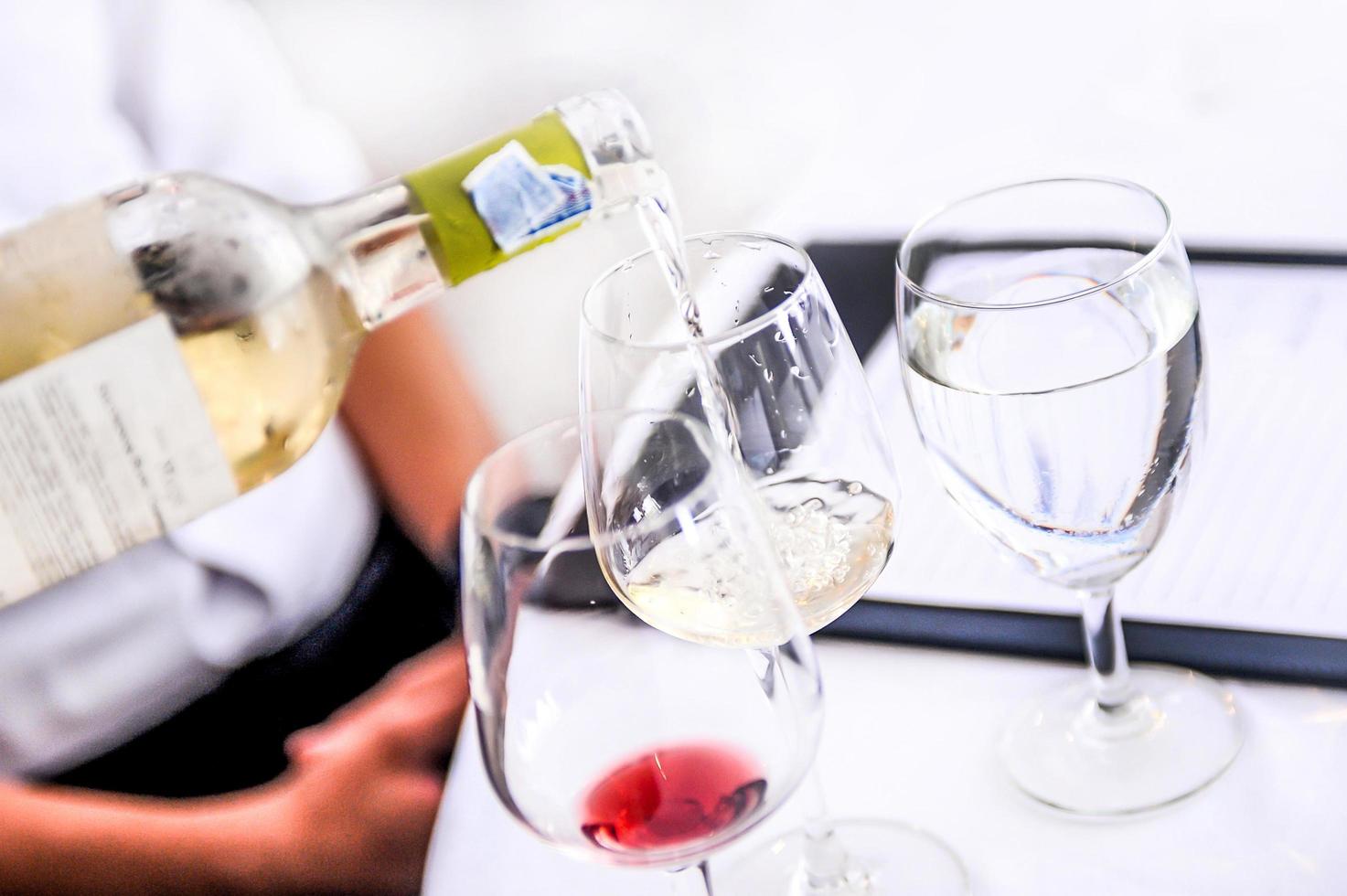 Verkostung von Weißwein in ein Glas gießen, Wein aus der Weinflasche einschenken foto