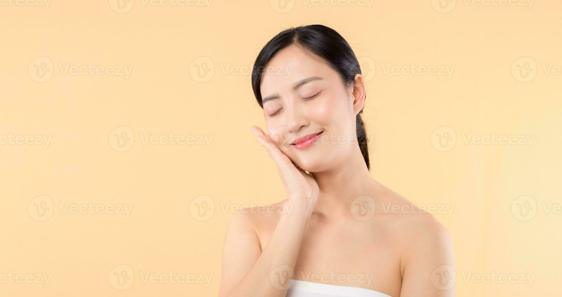 schön Mädchen asiatisch Modell- berühren frisch glühend hydratisiert Gesichts- Haut auf Beige Hintergrund Nahaufnahme. Schönheit Gesicht jung Frau mit natürlich bilden und gesund Haut Porträt. Haut Pflege Konzept foto