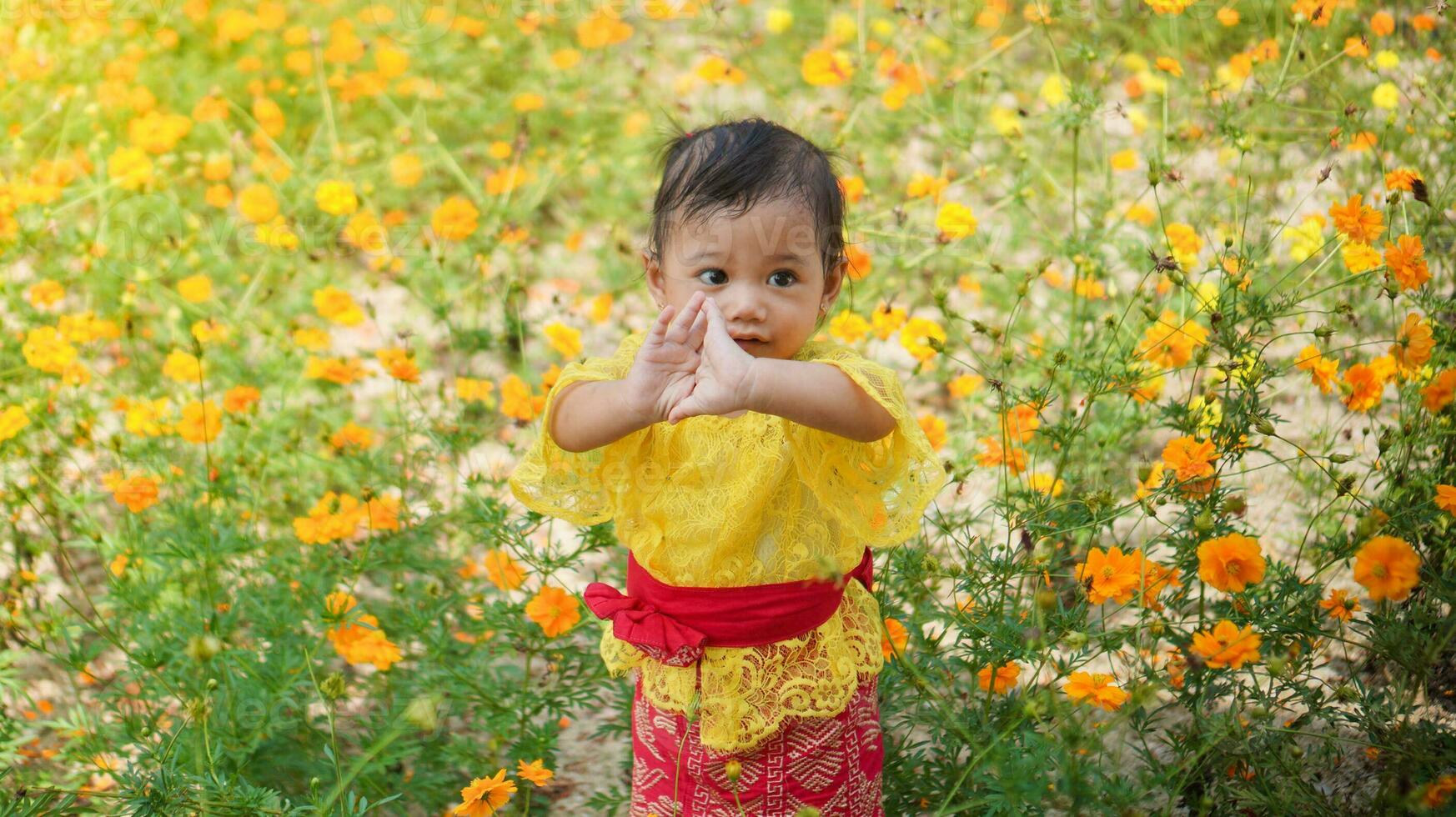wenig süß Mädchen tragen Gelb balinesisch Kleid spielen im Gelb und Weiß Blume Garten foto