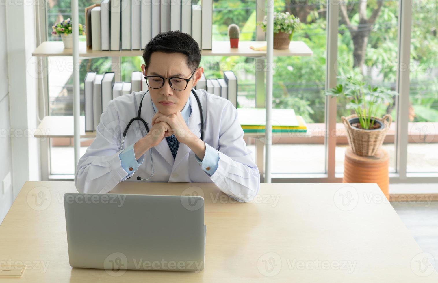 junger asiatischer Arzt, der Computer im Krankenhausbüro verwendet foto