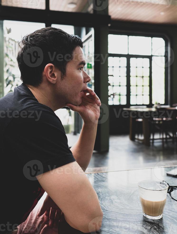 Porträt des jungen hübschen kaukasischen Mannes, der im Café sitzt foto